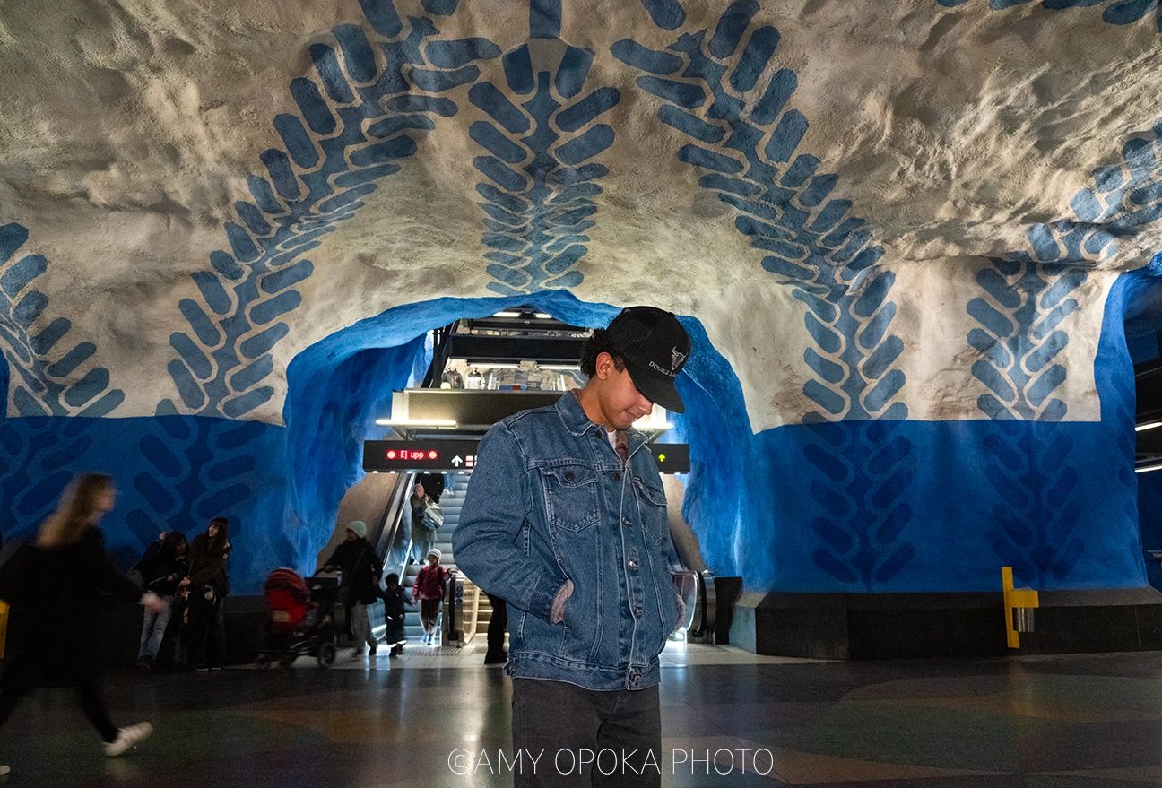 Man in denim jacket stands in a vibrant, blue-patterned underground station.