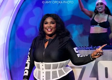 Confident woman in black outfit with white corset smiling on stage.