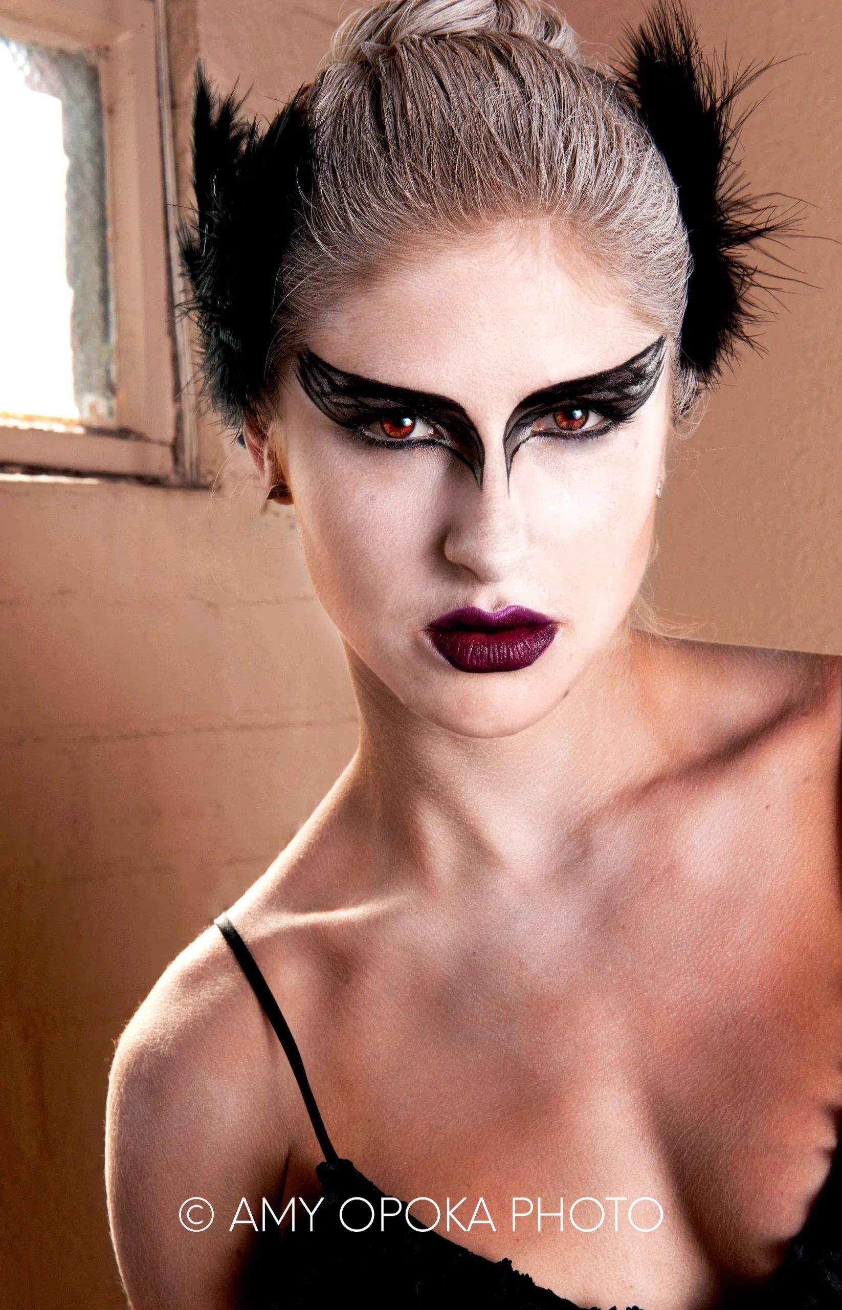 Woman with dramatic black feather eye makeup and dark lipstick.