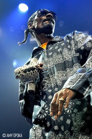 Snoop Dogg performing on stage with sunglasses and patterned attire.