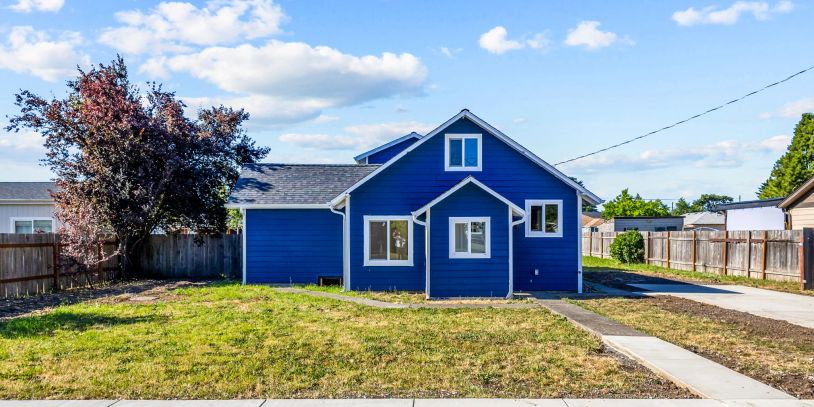 Blue house with a lawn and tree under a partly cloudy sky.