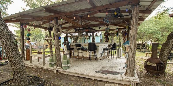 A rustic wooden bar covered with a roof, featuring chairs and a table, ideal for outdoor gatherings.