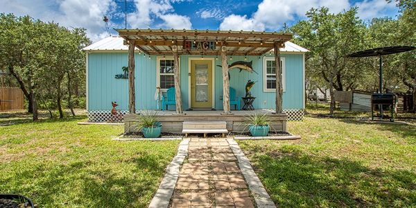 A cozy blue cabin with a porch and a lush yard, embodying a peaceful and inviting setting.