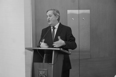 Man in suit speaking at podium with microphone in formal setting.