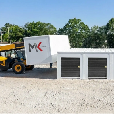 A forklift placing a white container with MK logo onto storage units outdoors.