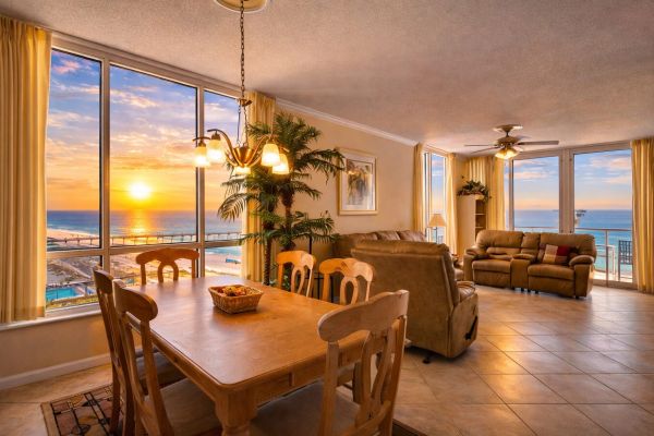 Dining room with wooden table and chairs overlooking a sunset beach view.