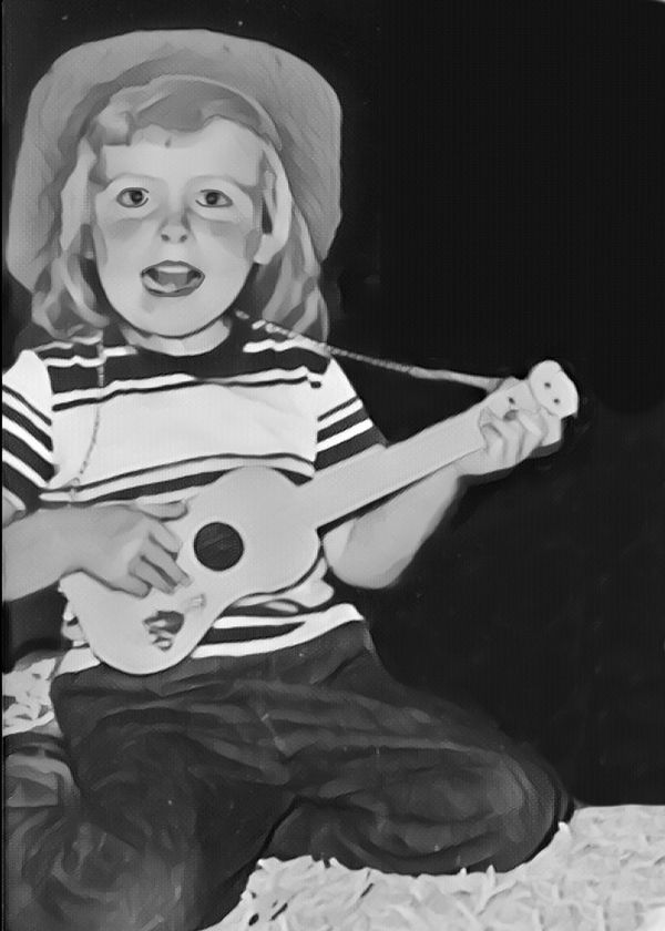A young child playing a small guitar and singing joyfully.