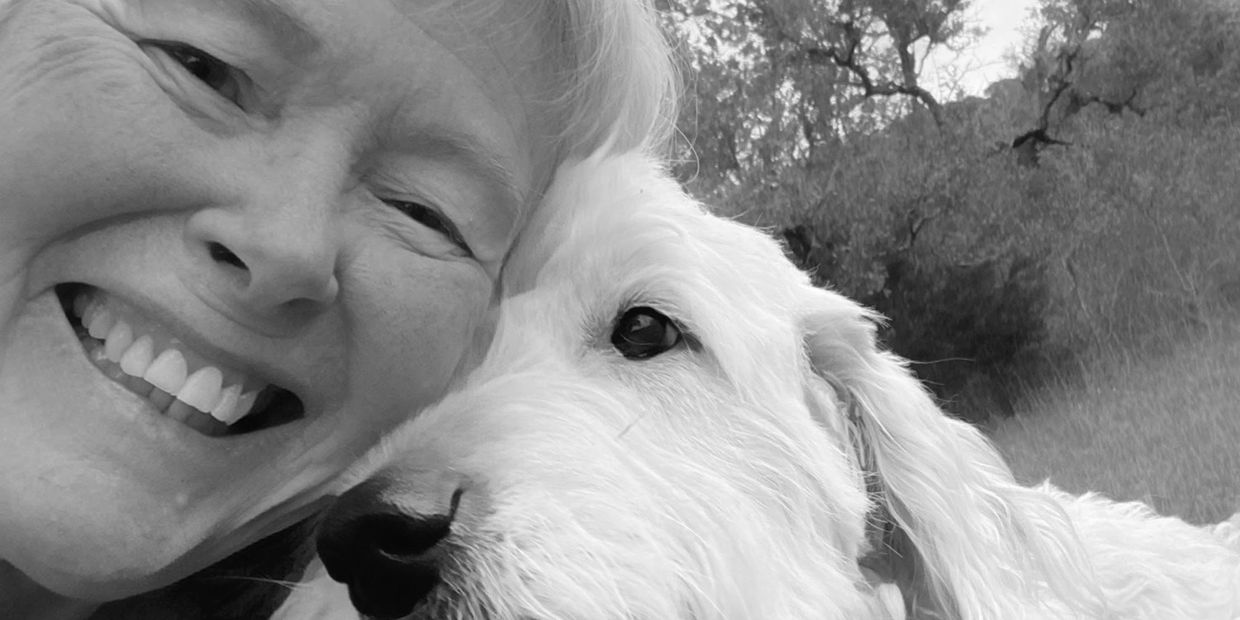 Close-up of a smiling woman with a white dog outdoors.