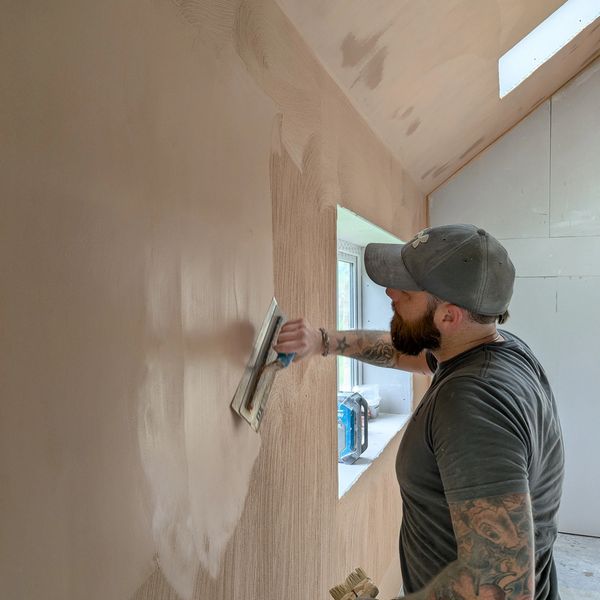 Man plastering a wall in a room under construction.
