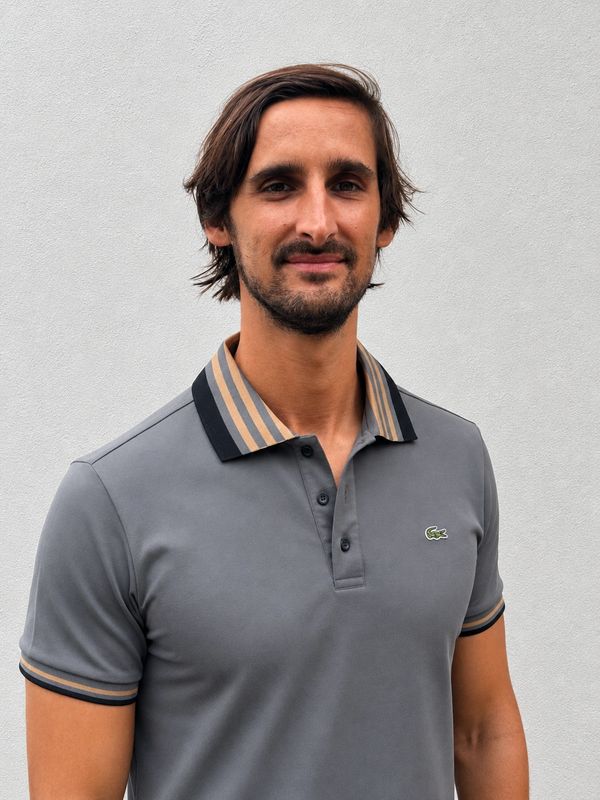 Man wearing a grey Lacoste polo shirt standing against a plain background.