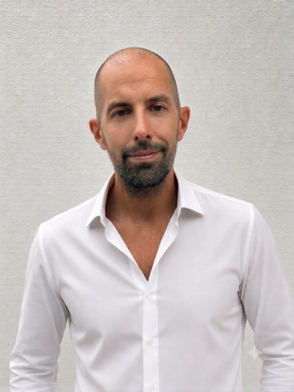 Hombre calvo con barba y camisa blanca.