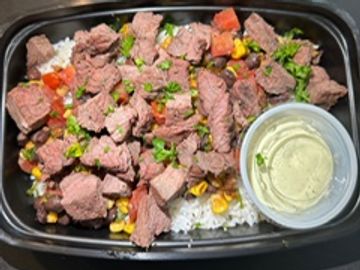 Beef and vegetable rice bowl with a side of sauce in a black container.