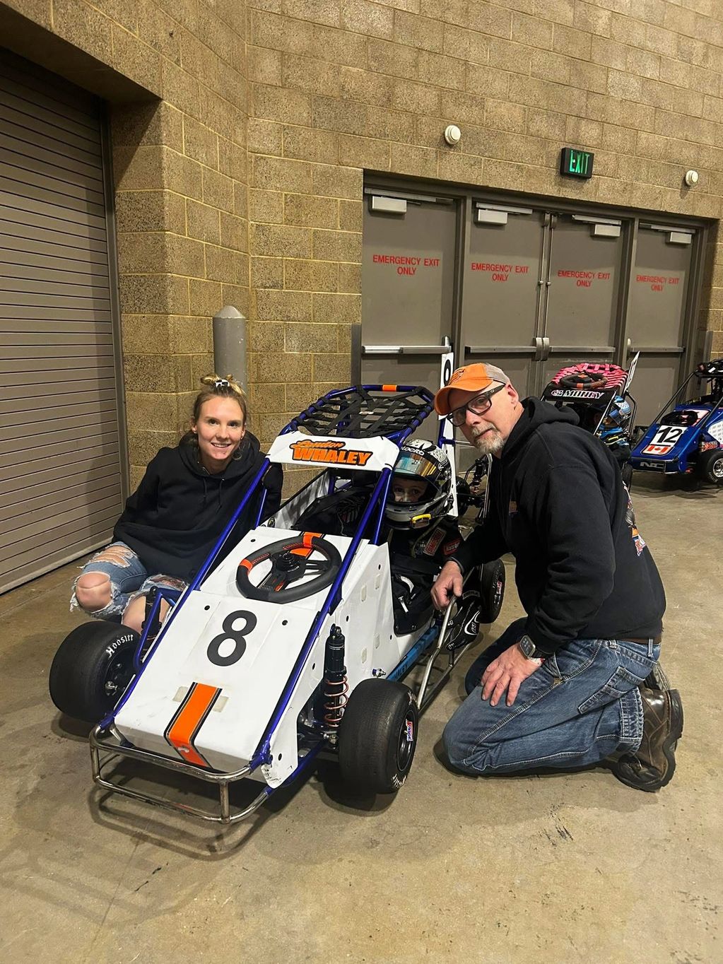 Family gathered around a small go-kart with a young driver inside.