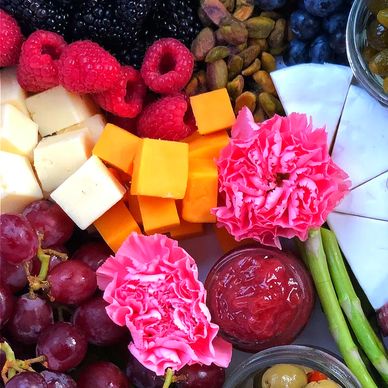Colorful charcuterie board with fruits, cheeses, nuts, and edible flowers.