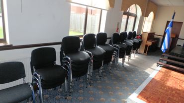 Row of stacked black chairs in a room with windows.