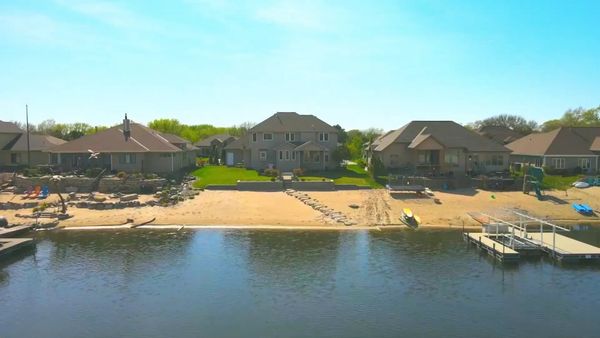 A lakeside view of houses with docks and sandy beaches on a sunny day.