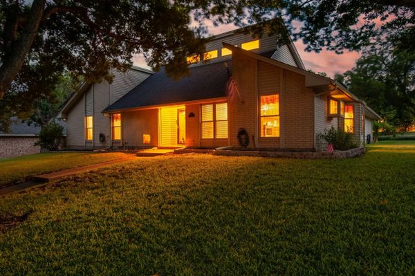 A warmly lit house at dusk with a well-maintained lawn and trees.