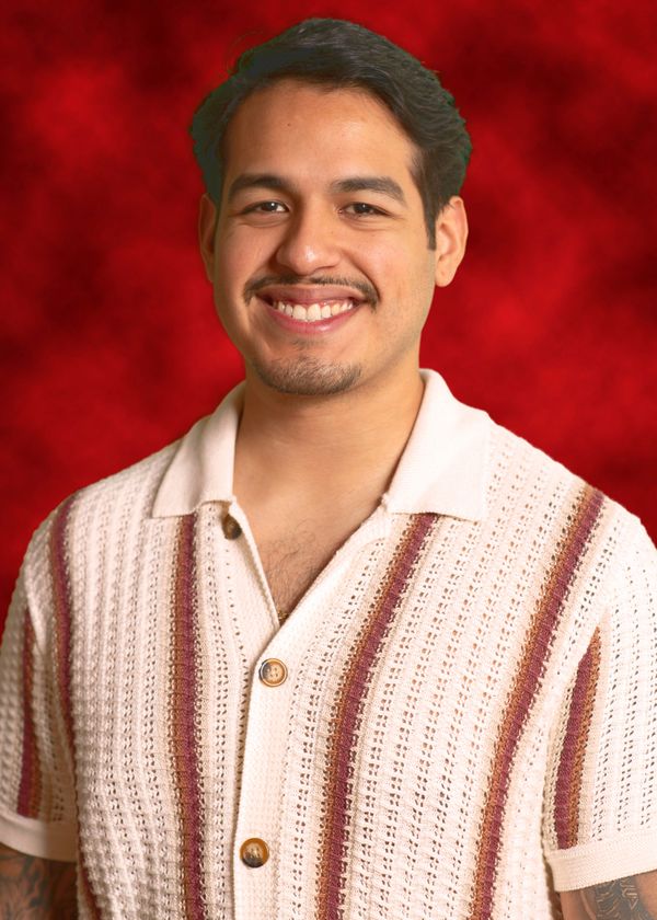 A smiling man in a textured striped shirt against a red background.
