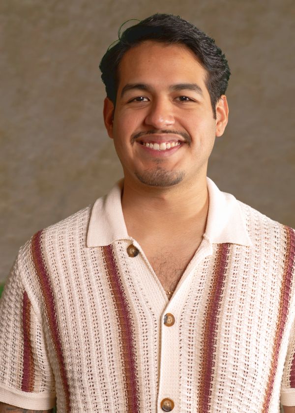 A smiling man wearing a striped knit shirt against a neutral background.