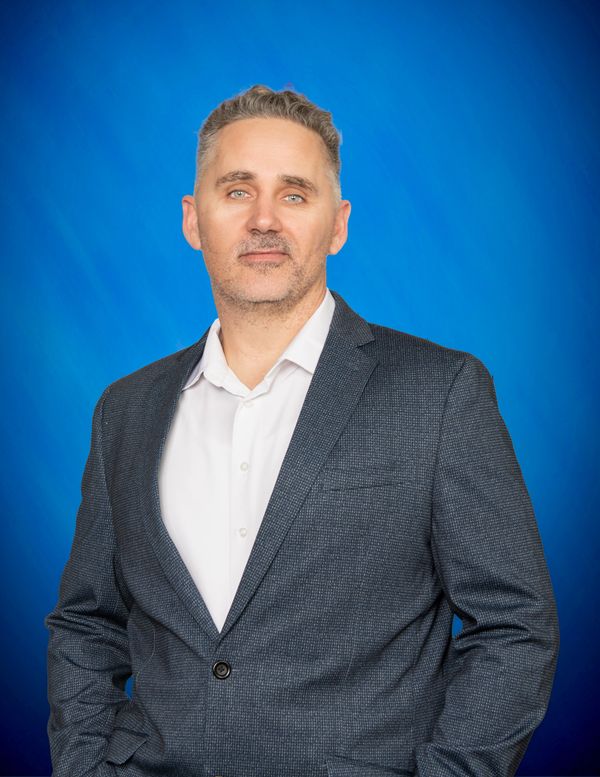 Confident man in a gray blazer against a blue background.