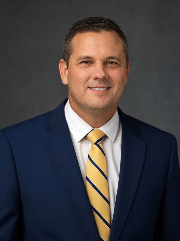 Man in a blue suit and yellow striped tie smiles.