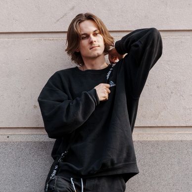Young man in black sweatshirt posing against a wall.