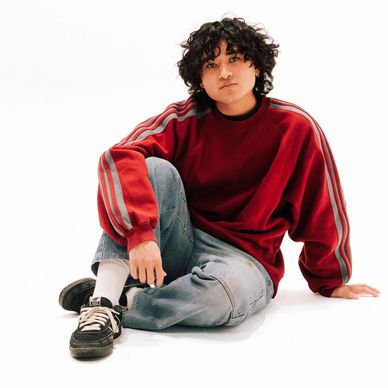 Person in a red sweatshirt and jeans sitting on the floor against a white background.