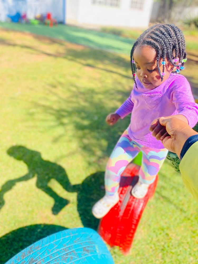 A child holding hands while balancing on colorful playground tires outside.