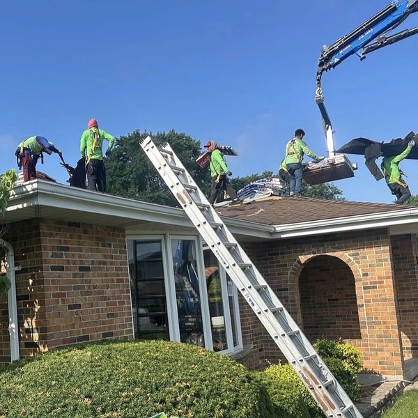 Workers removing old roofing materials from a house under clear blue skies.
