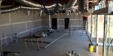 Interior of a building under construction with exposed ducts and a worker on a ladder.