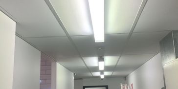 A well-lit hallway with cleaning supplies and a safety cone at the end.