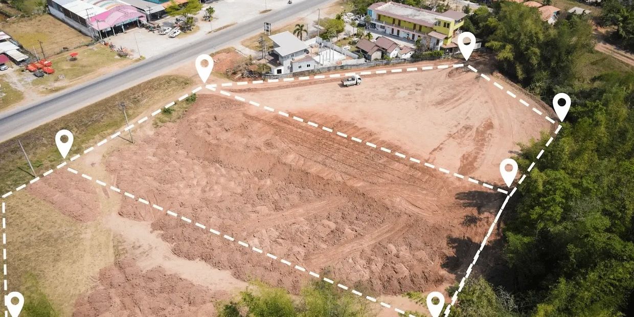 Aerial view of a marked vacant plot of land near a road and buildings.