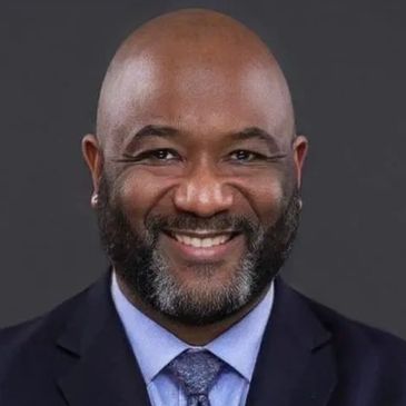 Smiling man in suit and tie with a neatly trimmed beard.