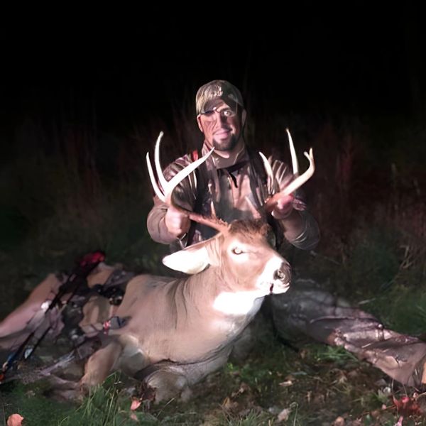 Hunter posing with a large buck deer at night.