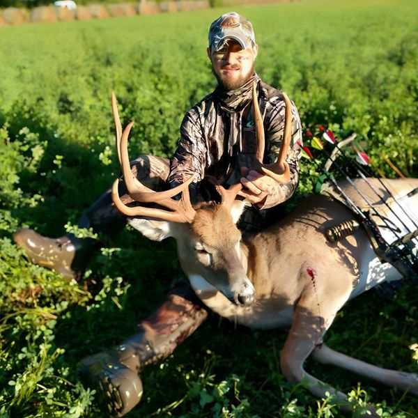 Hunter posing with a large buck deer in a green field.