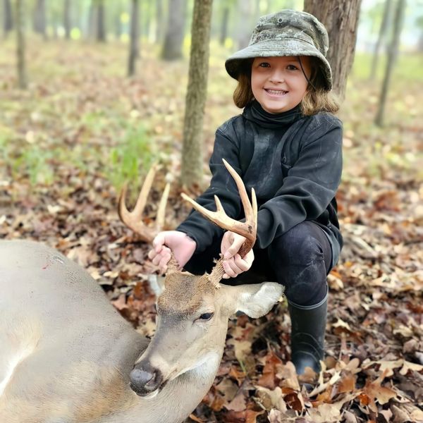 A young girl proudly holding a deer's antlers in a forest.