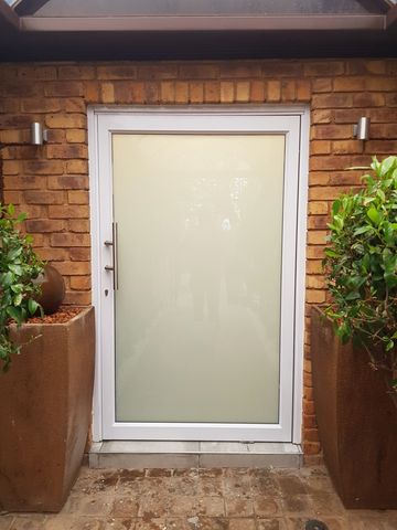 White Aluminium pivot door with translucent glass and stainless steel handle.