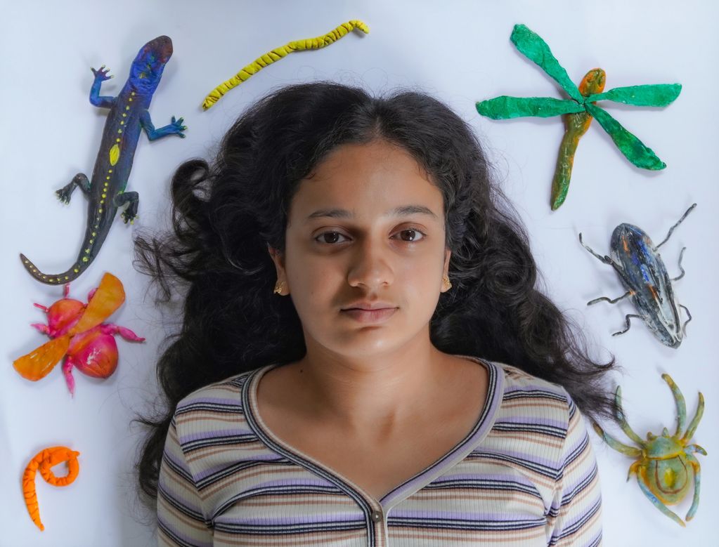 Young woman lying amidst colorful clay insect and animal sculptures.