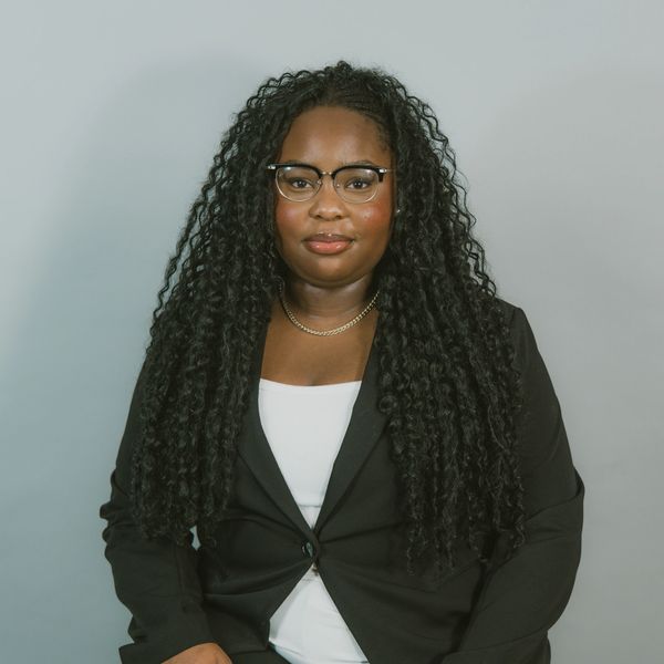 Confident woman with long curly hair wearing glasses and a black blazer.