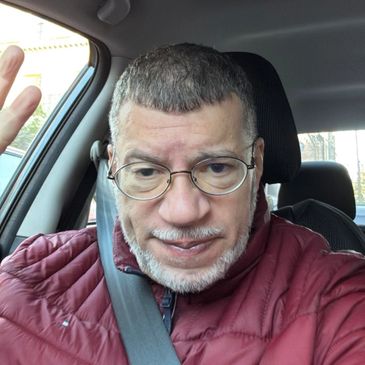 Man in glasses and red jacket waving inside a car.