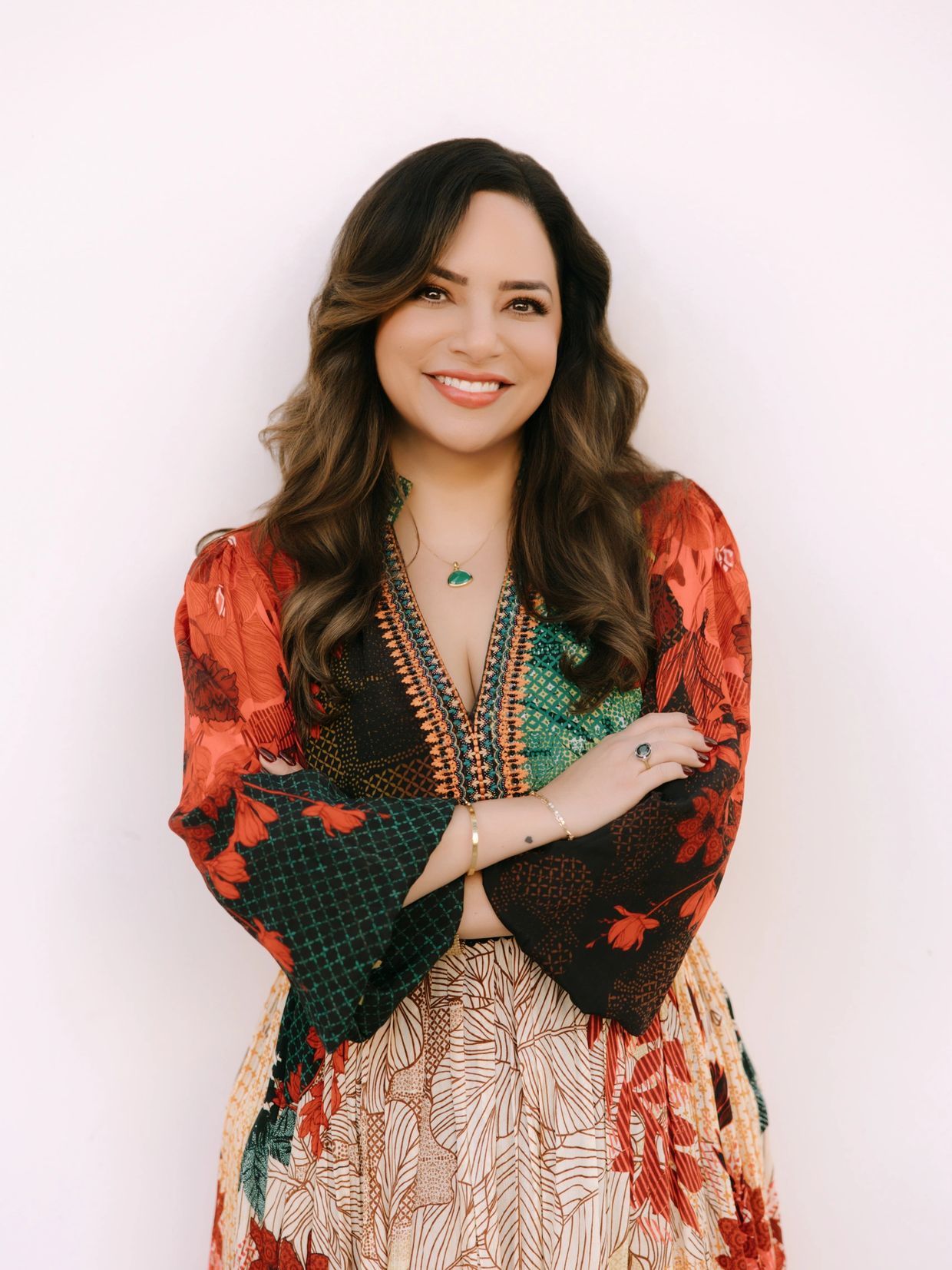 Smiling woman in a colorful, patterned dress with arms crossed.