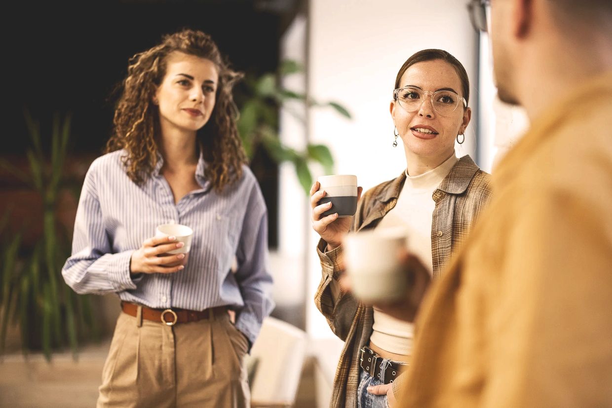 Three colleagues chatting and drinking coffee in a casual setting.