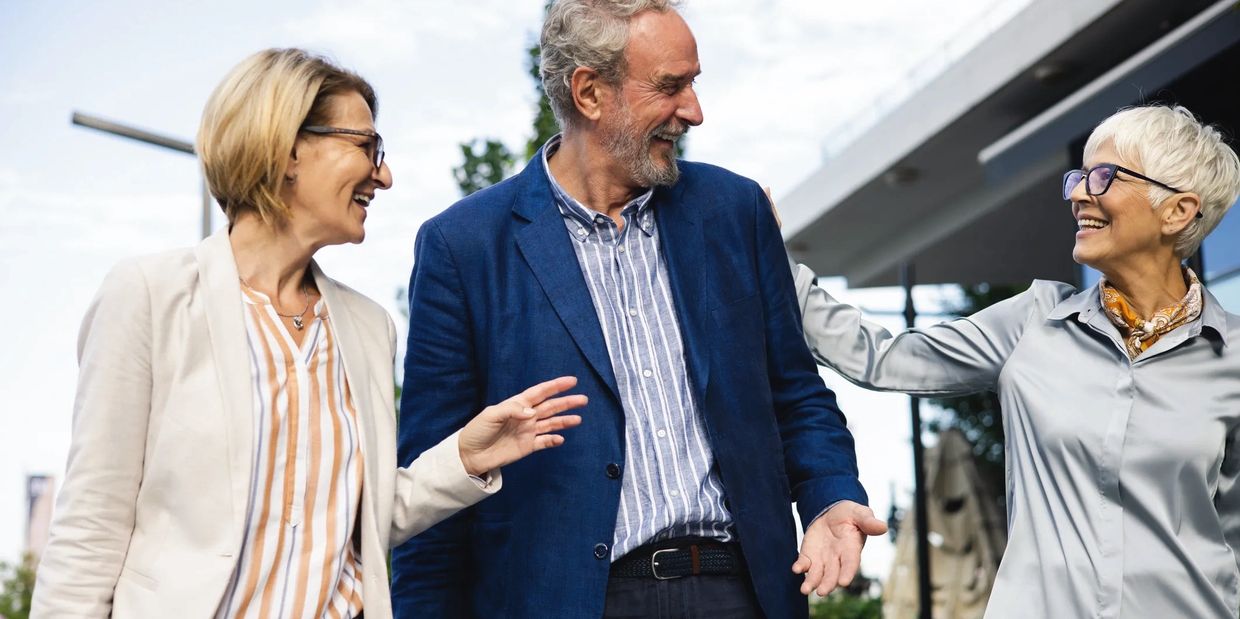 Three older adults happily chatting outdoors, enjoying each other's company.
