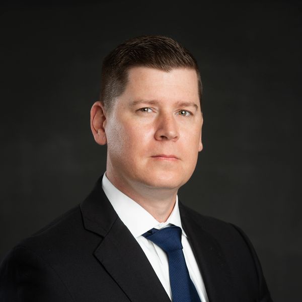 Professional man in a suit with a serious expression against a dark background.