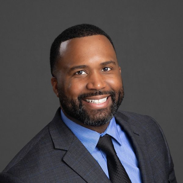 Smiling professional man in a suit and tie against a gray background.