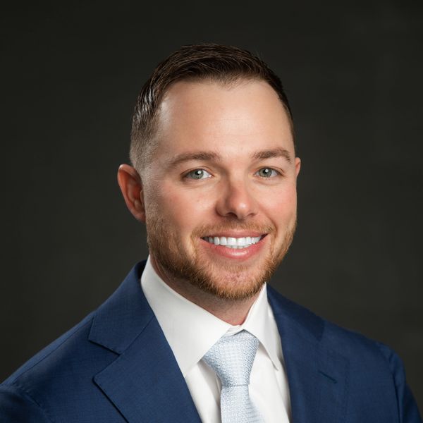 Smiling man in a blue suit and white tie against a dark background.