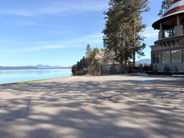 A peaceful lakeside view with a building and trees casting shadows on the pavement.