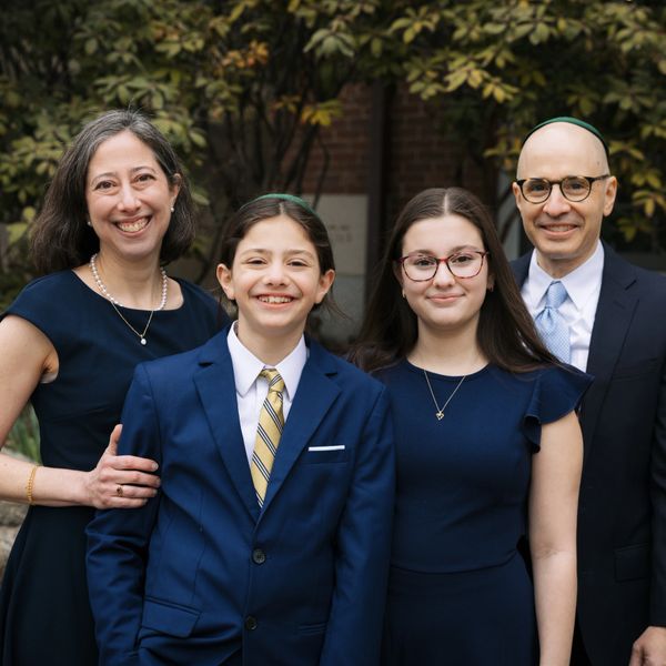 A smiling family dressed formally in blue, posing outdoors with greenery in the background.