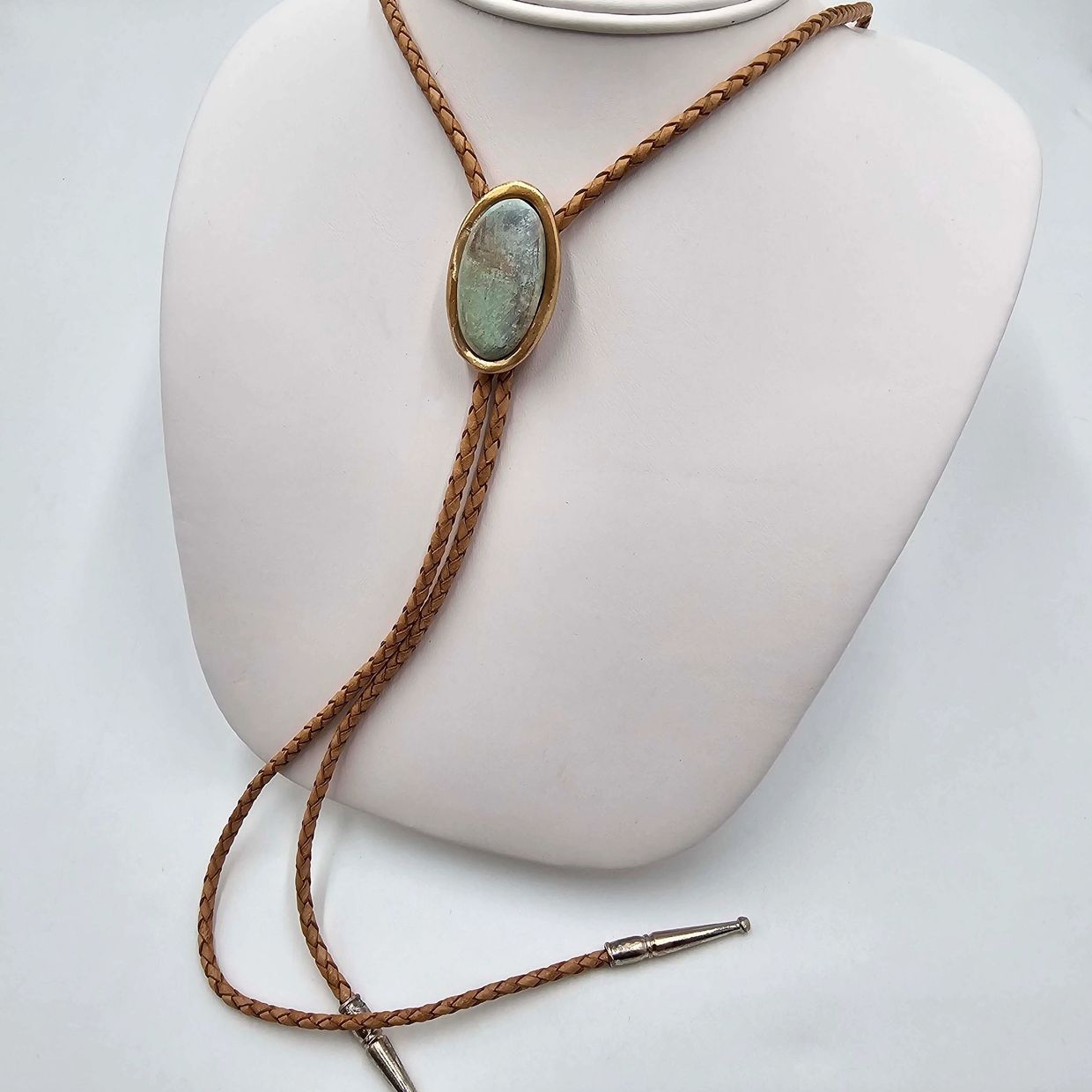 Braided leather bolo tie with oval stone centerpiece in gold setting.