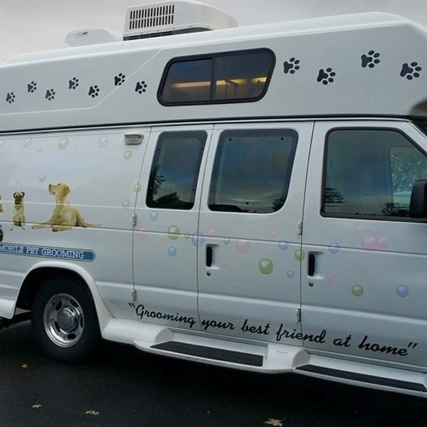 Mobile pet grooming van with dog images and paw prints.